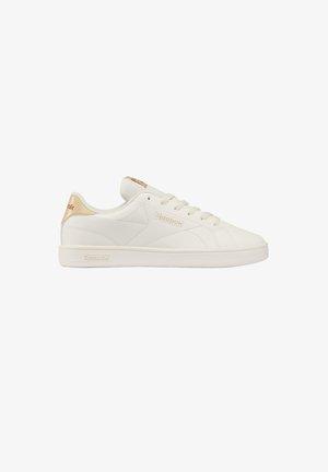 White low-top Reebok sneaker with beige accents on heel and logo, lace-up closure, and a clean rubber sole, side view.