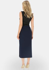 Czarny top bez rękawów w połączeniu z dopasowaną granatową spódnicą midi. Spódnica ma boczny rozcięcie, noszona z beżowymi szpilkami.