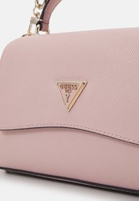 Różowa torebka teksturowana z złotym trójkątnym logo, charakteryzująca się gładką powierzchnią i zakrzywionymi liniami akcentującymi u podstawy. W zestawie regulowany pasek.