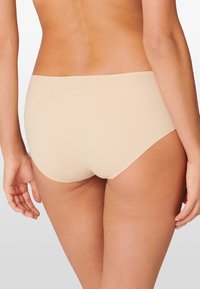 String beige senza cuciture con una texture liscia e un design a gamba alta, caratterizzato dall'assenza di cuciture visibili per una vestibilità discreta.