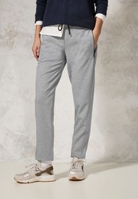 Ljusgrå sweatpants med tapered passform och elastisk midja. Har sidofickor och ett texturerat, mjukt material. Bärs med beige sneakers.