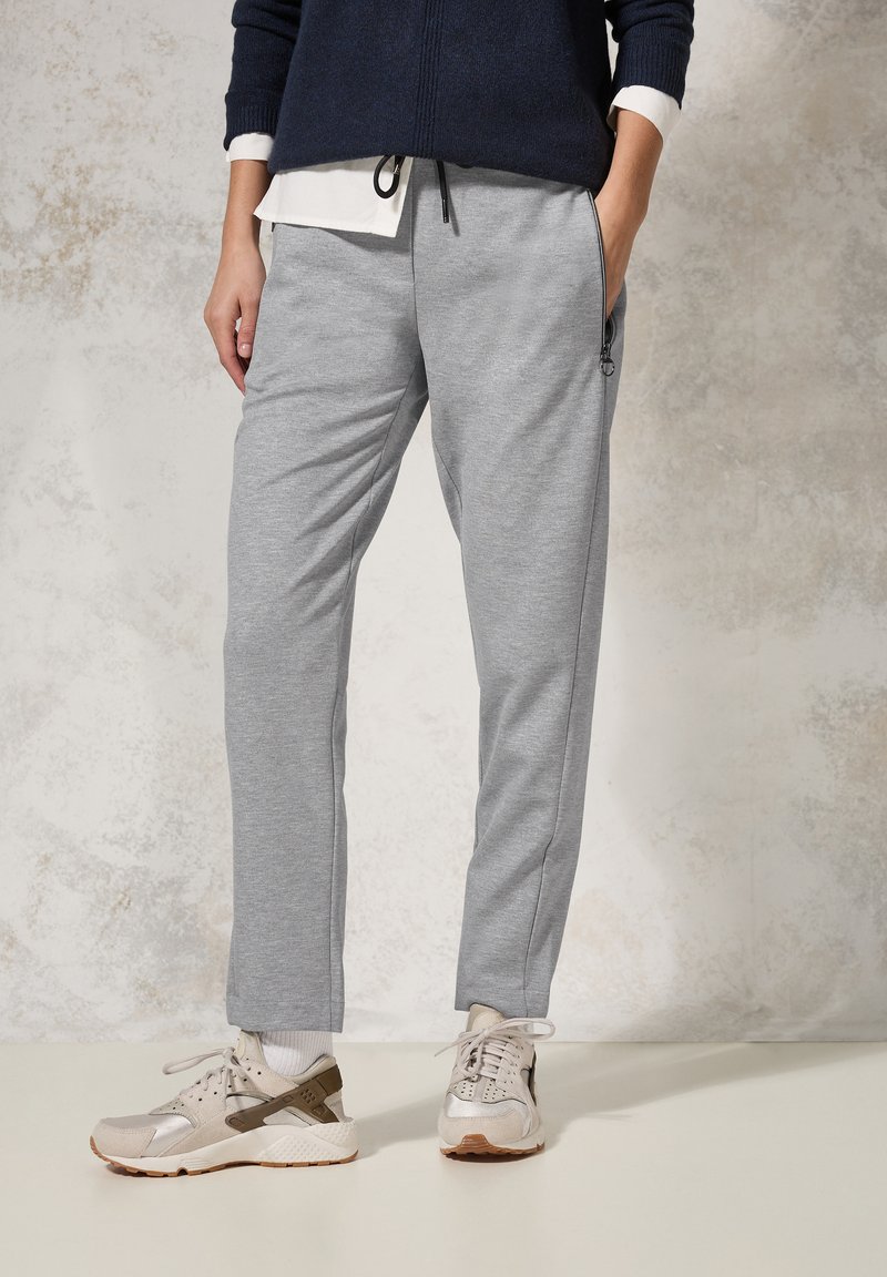 Ljusgrå sweatpants med tapered passform och elastisk midja. Har sidofickor och ett texturerat, mjukt material. Bärs med beige sneakers.
