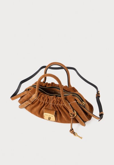 Pruun seemisnahast käekott kortsustatud disainiga, nähtavad kuldsed detailid, kaks käepidet ja eemaldatav must rihm. Ülal lukuga sulg.