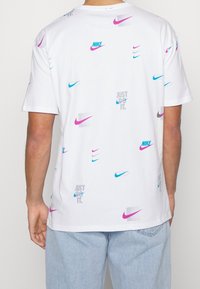Camiseta de algodón blanca con un patrón repetido de varios logotipos de Nike en rosa y azul, con el texto "Just Do It" en gris.