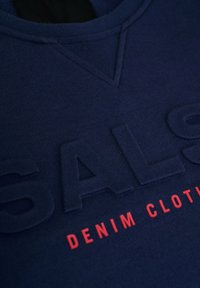 Sudadera azul marino con un logo texturizado "SAL" y el texto "DENIM CLOTHING" en rojo. Presenta un cuello redondo y puños de canalé finos. Material suave de algodón.