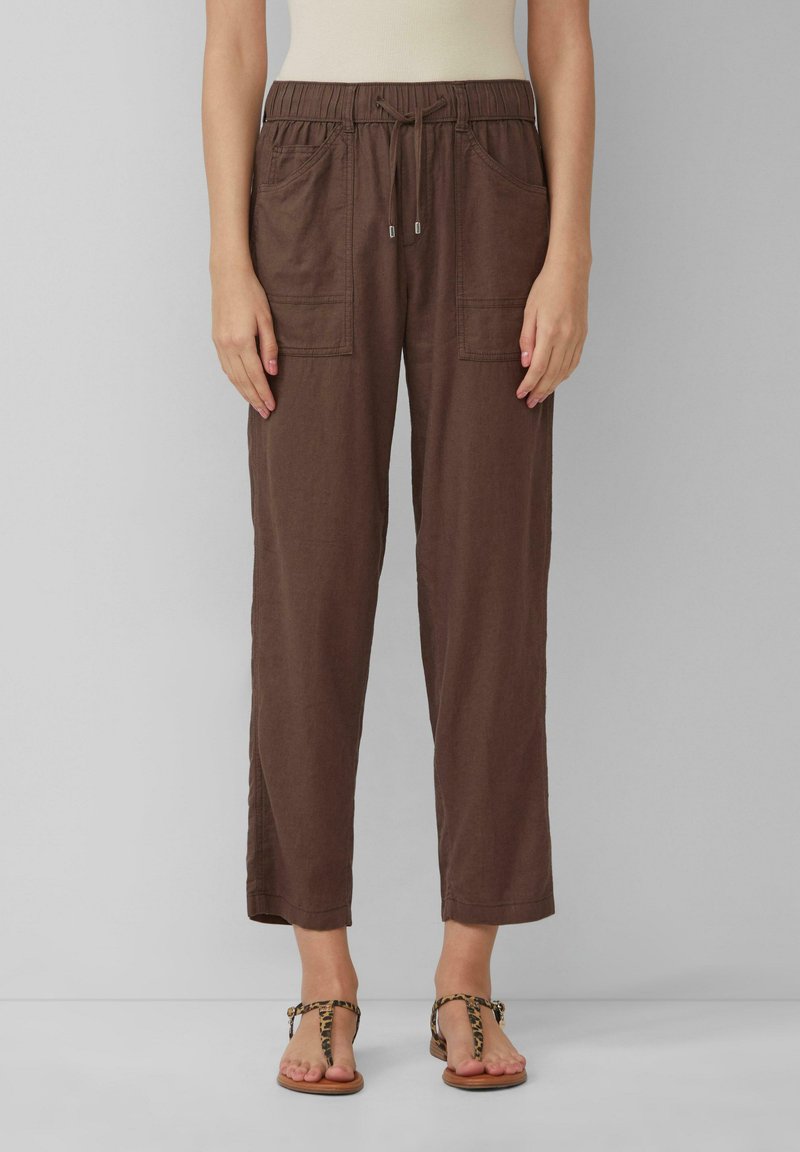Pantalon en mélange de lin marron avec une taille élastique, un cordon de serrage et deux poches à l'avant. Associé à des tongs à imprimé animal couleur fauve.