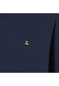 Marineblauwe kledingstuk van een gestructureerde stof; heeft een klein geborduurd geel en paars logo nabij de borst.