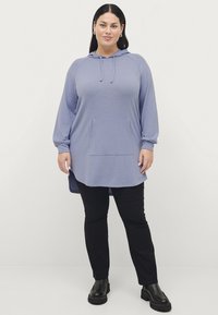 Lila lange mouwen hoodie tuniek met een voorkant zak, losse pasvorm en ribgebreide manchetten, gecombineerd met zwarte broek en chunky zwarte laarzen.