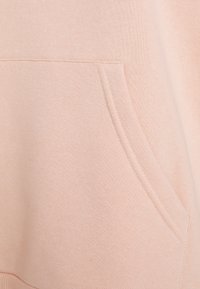 Felpa leggera rosa con tasca a marsupio, orlo a costine e texture morbida con dettagli cuciti lungo le cuciture.