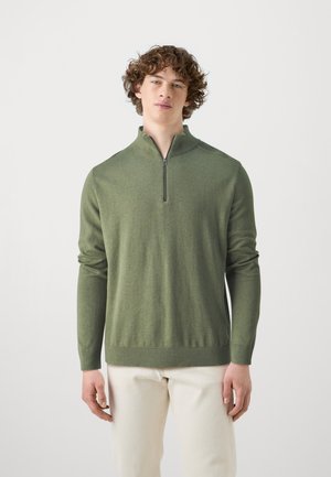 Green zip-up sweater made of a soft fabric, featuring long sleeves, ribbed cuffs, and a straight hem. Model stands against a neutral background.