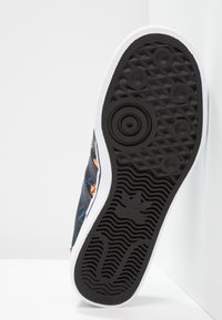 Svart sneaker sula med texturerat grepp, med en vit mellansula och färgglada blommönster på en canvasöverdel.