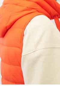 Puffy ärmellose Jacke in leuchtendem Orange mit Kapuze, kombiniert mit einem cremefarbenen Langarmoberteil. Verfügt über eine schlanke Nahtführung und Textur.