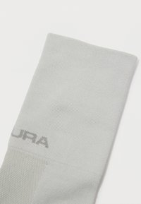 Artimas šviesiai pilko tekstūruoto audinio rankovės vaizdas su tamsesniu logotipu, esančiu šalia rankogaliai, ant balto fono.