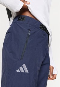 Αθλητικό παντελόνι σε ναυτικό μπλε χρώμα με υφή υφάσματος, φερμουάρ σε τσέπη στο πλάι και μαύρη μέση με λογότυπα της μάρκας.