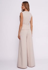 Beige ärmelloses Peplum-Top mit tailliertem Schnitt, kombiniert mit weit geschnittenen Hosen; glatte Textur und maßgeschneiderter Schnitt mit sauberer Silhouette.