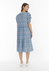 Rochie florală albastră cu mâneci bufante și fustă în straturi. Prezintă modele colorate pe o țesătură ușoară. Purtați cu teniși albi.