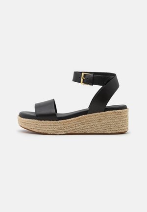 Sandales compensées en cuir noir avec une tige lisse, une bride de cheville réglable et une semelle plateforme en jute tressé. Détail accent en boucle dorée.