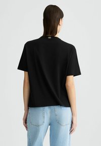 T-shirt nera a maniche corte con una vestibilità rilassata e un dettaglio del logo oro sul retro, abbinata a jeans azzurri a vita alta.