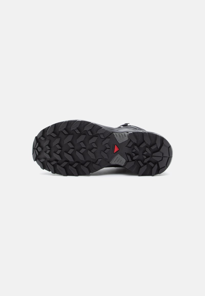 Zwarte rubberen zool met diepe profielpatronen voor grip, met een rode driehoekige accent en getextureerde secties voor extra houvast.