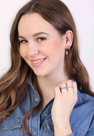 Silver hoop earrings with leaf charms, worn by a person in a denim shirt. Also features silver braided rings on the hand.