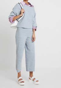Pull en tricot bleu clair avec des manches larges, associé à un pantalon cropped bleu clair et des sandales à plateforme blanches. Accessoire : petit sac blanc.