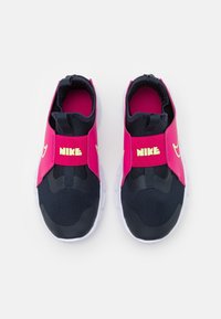 Sneakers Nike w różowym cholewce z czarnymi akcentami, z designem typu slip-on, z teksturowanej tkaniny i białą podeszwą. Jaskrawa logo na pasku.