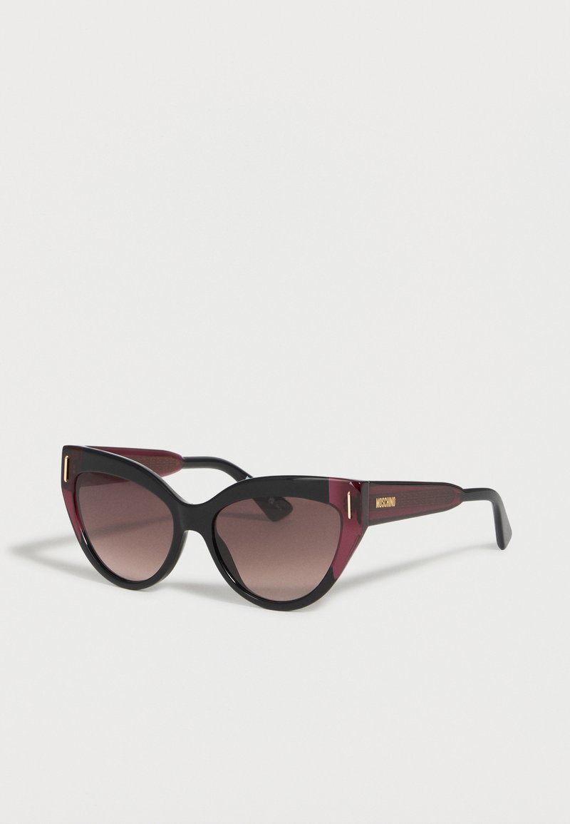 Cat-eye sunglasses with black and dark red frames and gradient brown lenses, featuring a gold Moschino logo on the temple.