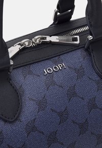 Sac à main bleu foncé avec un tissu texturé à motif, des accents en cuir noir, des accessoires en argent et un logo en évidence.