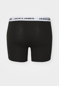 Schwarze Boxershorts mit einem weißen elastischen Bund, auf dem "JACK & JONES" in schwarzem Text steht. Glatte Textur, enganliegendes Design, Oberschenkellänge.