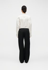 Pantalon long noir à coupe large, accompagné d'une chemise blanche à manches longues. Tissu lisse avec une coupe décontractée.