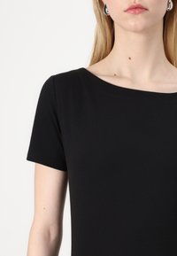 Svart kortärmad topp med rund halsringning. Slät textur och figurnära design. Synliga sömmar runt halsringningen och ärmarna.