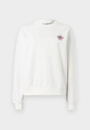 Hvit genser med rund hals, lange ermer og ribbestrikkede mansjetter. Har et rosa blomsterbroderi på venstre brystområde. Myk stof.