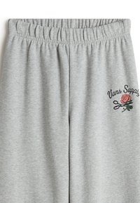 Grey sweatpants made of cotton blend with an elastic waistband. Features embroidered "Vans Supply" text and a rose design on the left side.