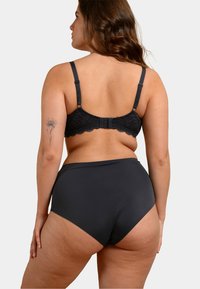 Soutien-gorge en dentelle noire avec bretelles réglables et fermeture à crochet, assorti à une culotte noire taille haute. Texture lisse, design simple.