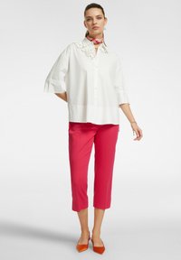 Camicia bianca a maniche corte, con bottoni frontali, dettaglio floreale sul colletto, abbinata a pantaloni cropped rosa e ballerine arancio a punta.
