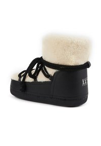 Bota de cuero negra con una parte superior de piel de oveja crema. Presenta cordones negros, punta redonda y un detalle del logo en el talón. Acabado texturizado.