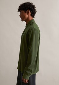 Pikend varrukatega oliivroheline särk nööbitava kraega, pehmest kangast, millel on lõdvestunud lõige ja sile tekstuur, esitatud küljelt.