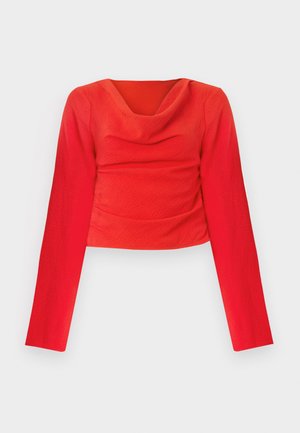 Punainen pitkähihainen lyhyt toppi, jossa on kauluskääntö. Sisältää teksturoitua kangasta ja poimutukset vyötäröllä, mikä luo istuvan siluetin.