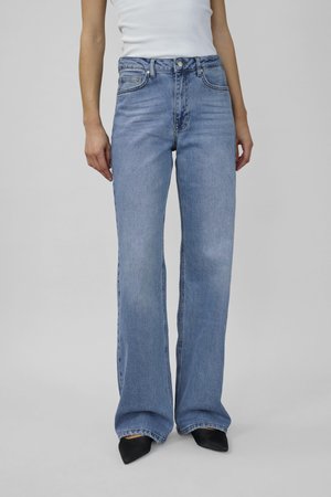 Light blue flared jeans with a high waist, two front pockets, and a faded wash. Smooth denim texture, paired with black pointed-toe shoes.