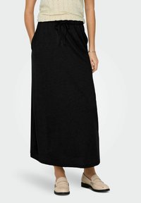 Zwarte, enkelvoudige rok met een elastische trekkoord tailleband en zijzakken, gemaakt van zachte, lichte stof, gecombineerd met beige instappers.