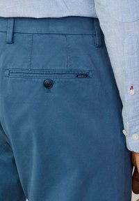 Jasnoniebieskie spodnie wykonane z bawełny o subtelnym połysku. Posiadają tylną kieszeń z zapięciem na guzik oraz małą metkę z logo marki.