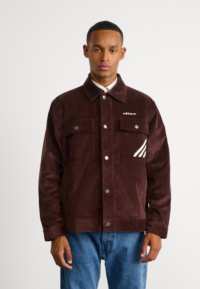 Burgundi värvi nõelkirjat jakk, millel on päästiknupud, kaks eespocketit ja valged Adidas triibud vasakul rinna taskul.