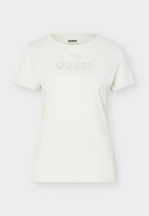 T-shirt blanc à manches courtes col rond avec petit logo « GUESS » en strass sur la poitrine, fond uni.