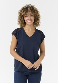 Haut à manches courtes bleu marine avec un col en V et des accents en dentelle sur les épaules. Tissu lisse avec une coupe décontractée.