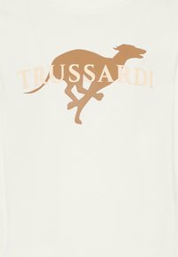 Witte T-shirt met een tan silhouet van een rennende hond en het "TRUSSARDI" logo in een zachte, lichte beige kleur. Glad katoen textuur.