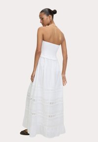 Abito lungo strapless bianco con parte superiore arricciata, parte inferiore fluente e dettagli decorativi in pizzo orizzontale. Tessuto morbido con una texture leggera.