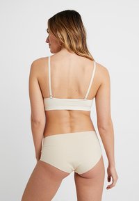 Μπεζ σου�τιέν και σετ εσώρουχων hipster. Μαλακό ύφασμα, μινιμαλιστικός σχεδιασμός, λεπτές τιράντες και ομαλή υφή χωρίς ορατές μεταλλικές λεπτομέρειες ή διακοσμήσεις.