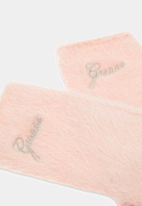 Guanti rosa morbidi realizzati in materiale soffice, con il logo "Guess" in corsivo argentato. La texture appare soffice e accogliente.