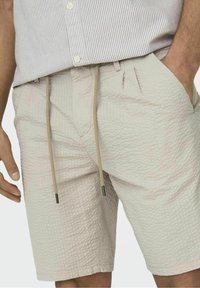 Vaaleanbeiget shortsit, jotka on valmistettu tekstuurikankaasta ja joissa on nauhavyötärö metallisilla päillä sekä sivutaskut.