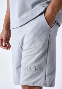 Shorts en coton gris avec poches latérales, arborant un logo brodé "Project x Paris" et une texture lisse. Coupe décontractée, longueur mi-cuisse.
